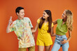 © LIGHTFIELD STUDIOS - joyous multicultural teenagers in vivid casual outfits looking at each other on orange backdrop