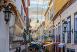 Fototapeta Fototapeta uliczki - A cable car gondola to the town of Monte passes over the famous Rua de Santa Maria narrow street of cafes, colorful doors and shops in the historic medieval old town of Funchal, Madeira Portugal.