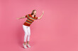 Full length profile photo of astonished cheerful girl look arm palm waving hi empty space isolated on pink color background