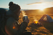 Young tourist holding metal enamel cup of hot steaming tea by an outdoor campfire. Drinking warm beverage by a bonfire. Scenic Icelandic nature.