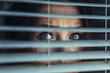 Terrified woman looking through window blinds outside. Privacy and intrusion concepts.