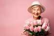 © Мария - Joyful, happy grandmother in a hat on a pink background with a bouquet of tulips, copy space