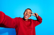 Photo of funky cheerful guy take selfie demonstrate v-sign eye wink blink isolated on blue color background
