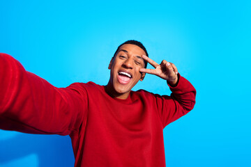 photo of funky cheerful guy take selfie demonstrate v-sign eye wink blink isolated on blue color bac