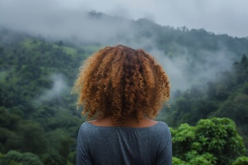 Wall Mural - Back view of a girl with curly hair overlooking a misty forest landscape