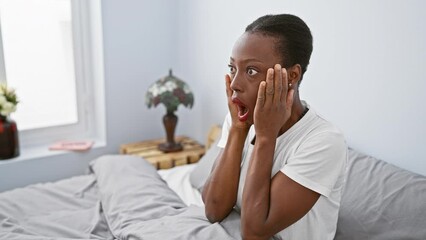 Wall Mural - Shocked african american woman lying in bed, expressive face full of amazement and fear, astonished and afraid in the comfort of her bedroom