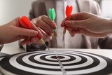 Fototapeta  - Business targeting concept. People with darts aiming at dartboard at table, closeup