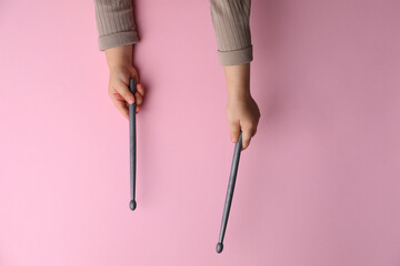 Wall Mural - Little kid holding drumsticks on pink background, top view