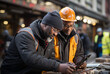 Two construction workers and engineers look at a laptop and discuss the working process. Two African-American male engineers standing near a building construction site.