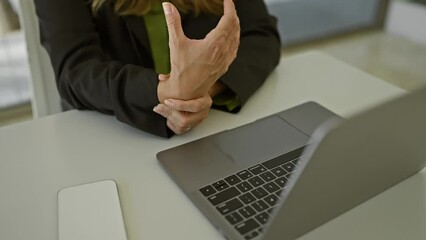 Sticker - A young hispanic woman experiencing wrist pain at her office desk with a laptop.