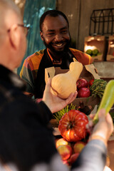 Wall Mural - Fresh products for elderly client at organic food market, man talking to vendor and shopping at local farmers market. Friendly farmer standing behind fruit and vegetable stall and serving customer.