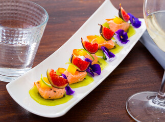 Wall Mural - Pieces of pickled salmon served on kiwi slices with figs, mango and kumquat garnished with pansy flowers