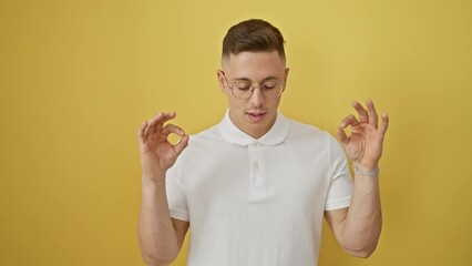 Poster - Chill hispanic guy in glasses strikes a zen yoga pose, eyes closed in blissful meditation - a vibrant yellow isolated background life concept