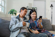© itchaznong - Retired elderly couple sits on couch drink tea and using mobile together and relax in their home. Senior Activity Concept