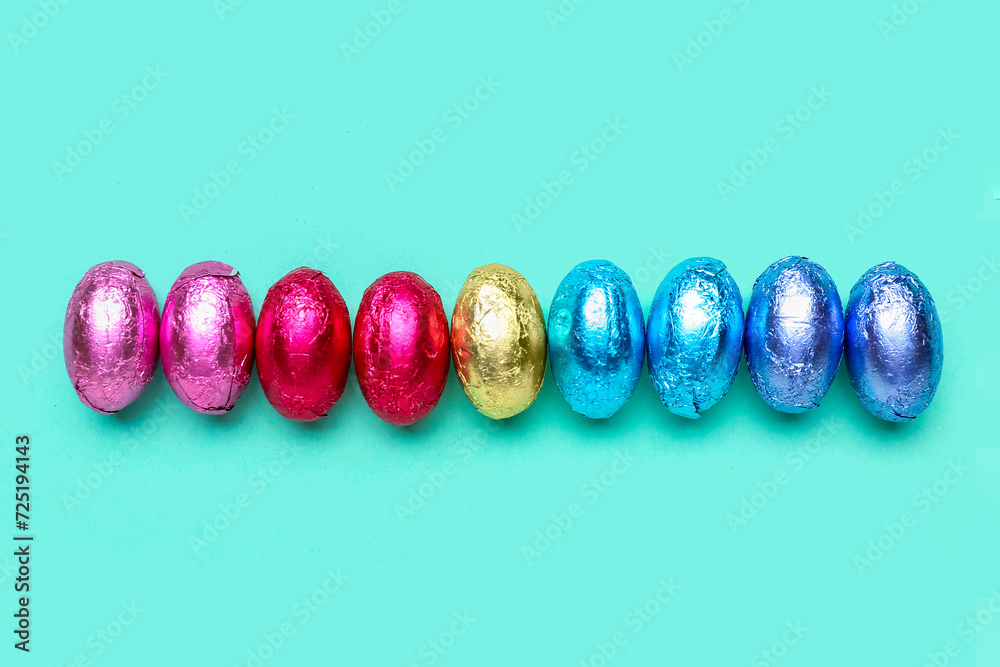 Row of chocolate Easter eggs in foil on color background