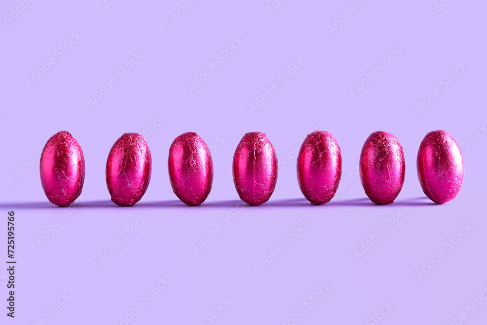 Row of chocolate Easter eggs in color foil on lilac background