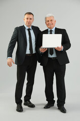 Wall Mural - Mature brothers in suits with laptop on grey background