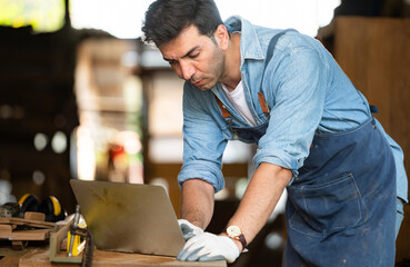 Carpenter working on laptop in his workshop at a woodworking factory