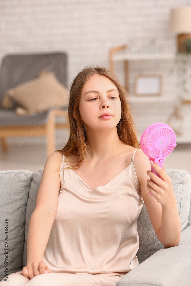 Beautiful young woman with handheld mini fan at home