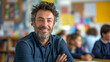 Portrait of smiling male teacher in a class at elementary school looking at camera with learning students on background. Happy smiling middle aged man  elementary or junior school male teacher 