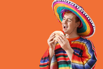 Canvas Print - Portrait of young Mexican man in sombrero eating taco on orange background