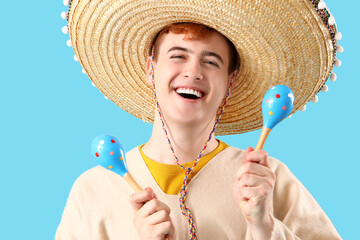 Wall Mural - Portrait of young Mexican man in sombrero and with maracas on blue background