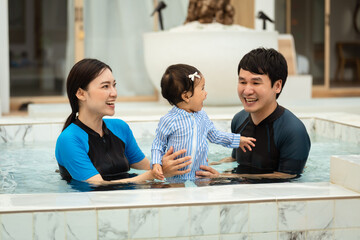 Wall Mural - happy family. father and mother with small daughter in swimming pool.