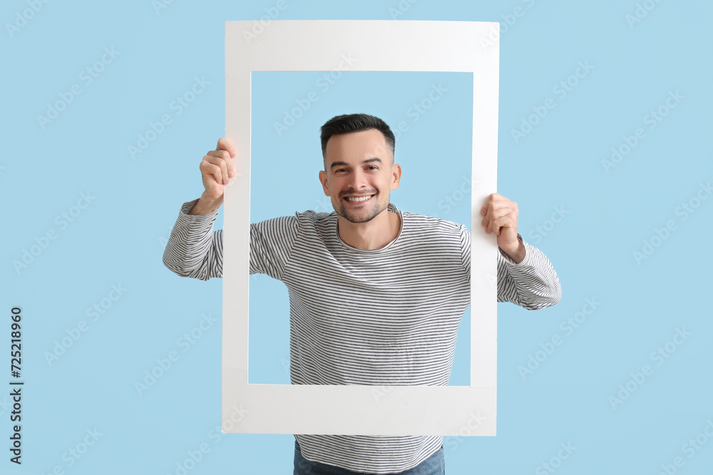 Happy young man with frame on blue background