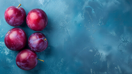 Wall Mural - Five fresh plums on a textured blue background with a place for text, suitable for healthy eating or culinary concepts