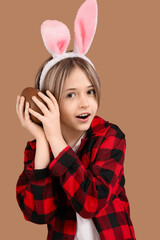 Poster - Cute little boy in bunny ears with chocolate egg on brown background. Easter celebration