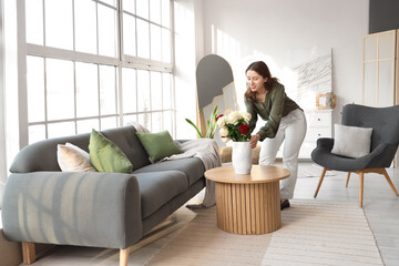 Wall Mural - Young woman putting vase with roses on table in living room