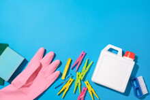 A Sponge, A Pink Rubber Glove, Colorful Clothespins, A White Detergent Bottle And A Brush Are Displayed In The Bottom Half Of The Frame Against A Blue Background. Free Space For Design.