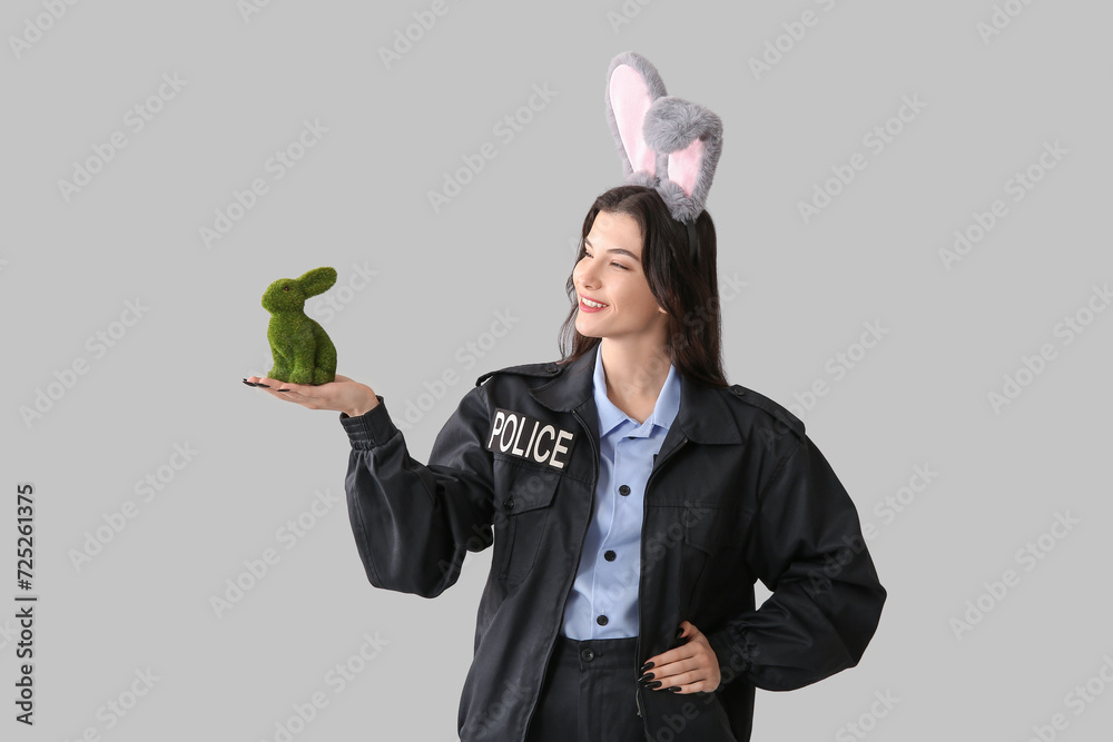 Female police officer in bunny ears with Easter rabbit on light background