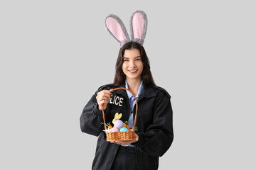 Poster - Female police officer in bunny ears with Easter eggs on light background