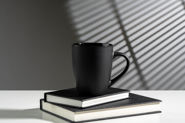 Sticker - Black cup on books in sunlight on gray background