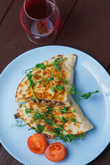 Two parts of pork quesadillas with tomato and pea stalks in blue plate on wooden table.Mexican tacos