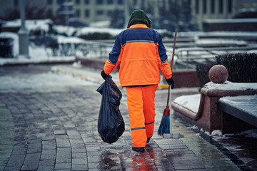 Wall Mural - Municipal worker sweeps street, janitor with broom and dustpan working during snow storm in the evening. Man in uniform with broomstick and scoop sweep city street in winter season, cleanup sidewalk