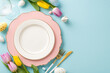 Festive Dining Scene: Overhead photo capturing an Easter-themed table setting with plate, cutlery, wine glass, tulips, ceramic bunny and colorful eggs. Pastel blue backdrop, perfect for text