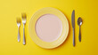 Top down view of a pink and yellow plate isolated on yellow background with fork spoon and knife with copy space