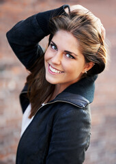 Portrait, beauty and happy woman with hair by brick wall in city outdoor alone. Face, fashion and hairstyle of confident young person, casual clothes and facial expression of girl in Switzerland