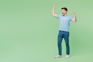 Wall Mural - Full body overjoyed fun excited young man wear blue t-shirt title volunteer do winner gesture clench fist isolated on plain green background. Voluntary free work assistance help charity grace concept.