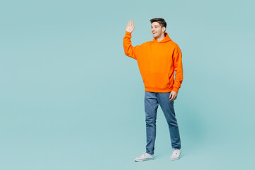 Wall Mural - Full body smiling happy young man he wears orange hoody casual clothes look camera walking going walk go isolated on plain pastel light blue cyan color background studio portrait. Lifestyle concept.