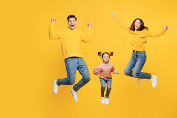 Full body young happy overjoyed parents mom dad with child kid girl 7-8 years old wear pink sweater casual clothes jump high do winner gesture isolated on plain yellow background. Family day concept.