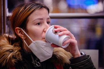 Wall Mural - Masked Commuter Drinking Coffee. Woman in a face mask sipping coffee on public transit