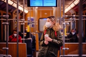 Wall Mural - Masked Woman with Coffee in Train. Young woman with mask holding coffee cup in train