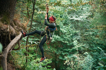 Wall Mural - Focused on the climbing up. Woman is in the forest, using the safety equipment