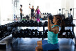 © Wavebreak Media - Side view of biracial young woman lifting dumbbells while sitting in health club, copy space