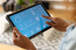 © Wavebreak Media - Hands of biracial woman in living room at home using tablet with smart home interface on screen