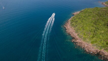 Wall Mural - Aerial view of a speedboat cruising near a lush green coastline, leaving a white wake in the turquoise sea