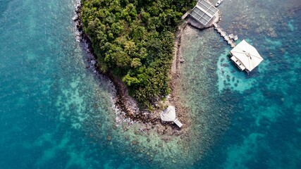 Wall Mural - Aerial view of a tropical island with lush greenery surrounded by a crystal-clear coral sea, featuring a small pier and pavilion, ideal for travel or vacation concepts